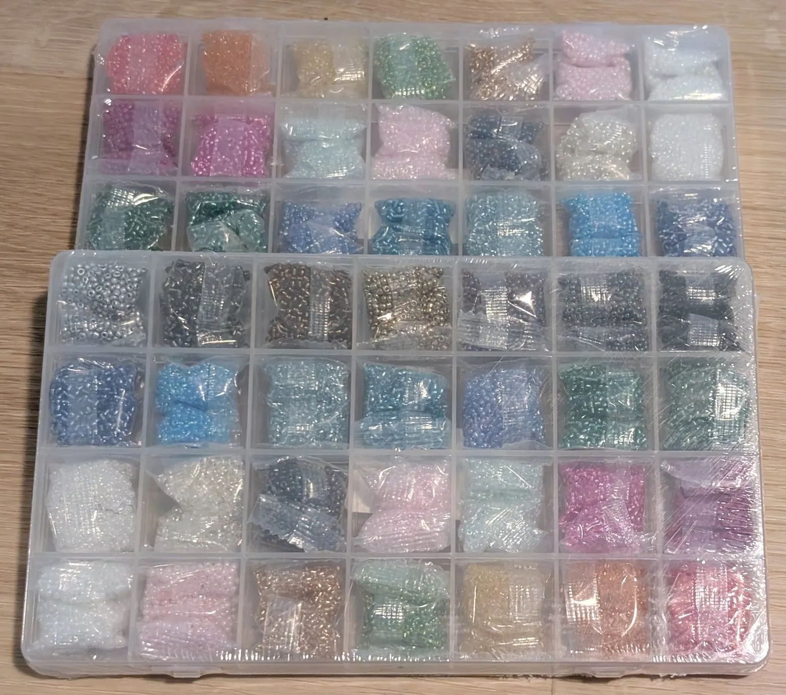 Two clear organizer boxes of seed beads, dozens of bags sorted by color in a grid.
