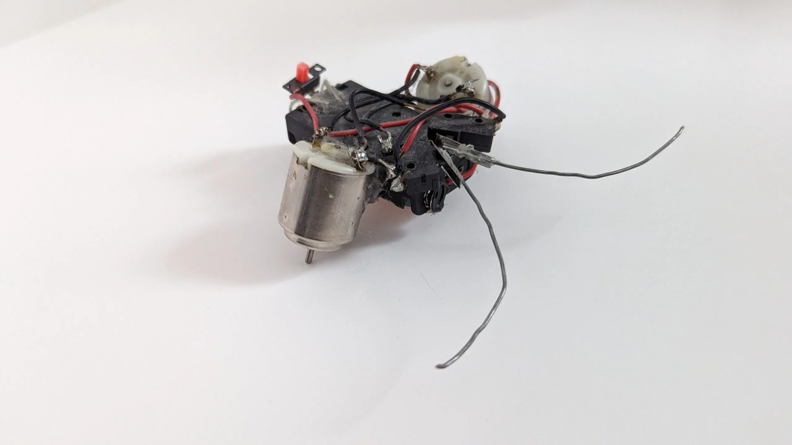 Three-quarter view of a Beetle: two toy motors on a battery-holder chassis, red power switch on top, bent wire feelers