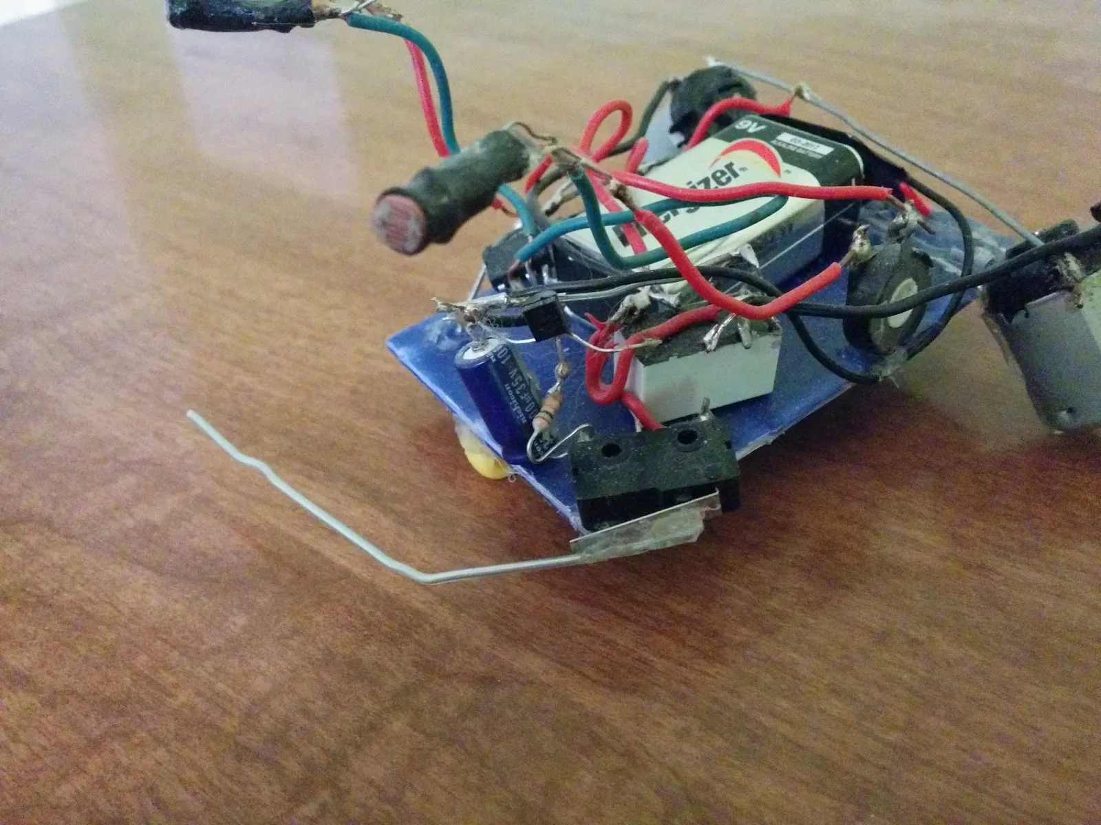 Herbie the Photovore, older bench photo: 9V battery on a blue plastic chassis, photoresistor eyes on stalks, wire whisker out front