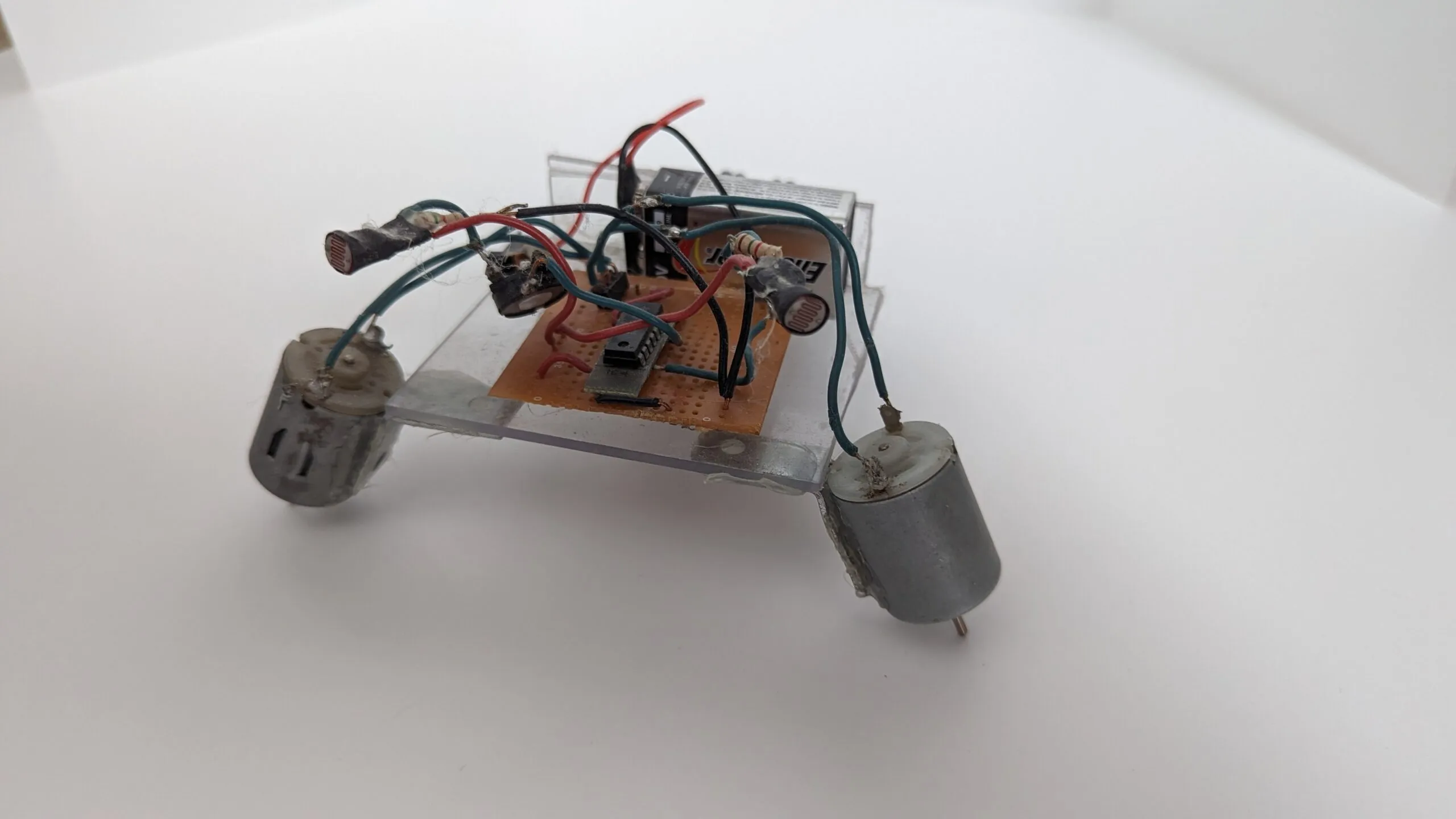NoBB from the side: photoresistors arcing over the protoboard on long leads, motors angled down as legs