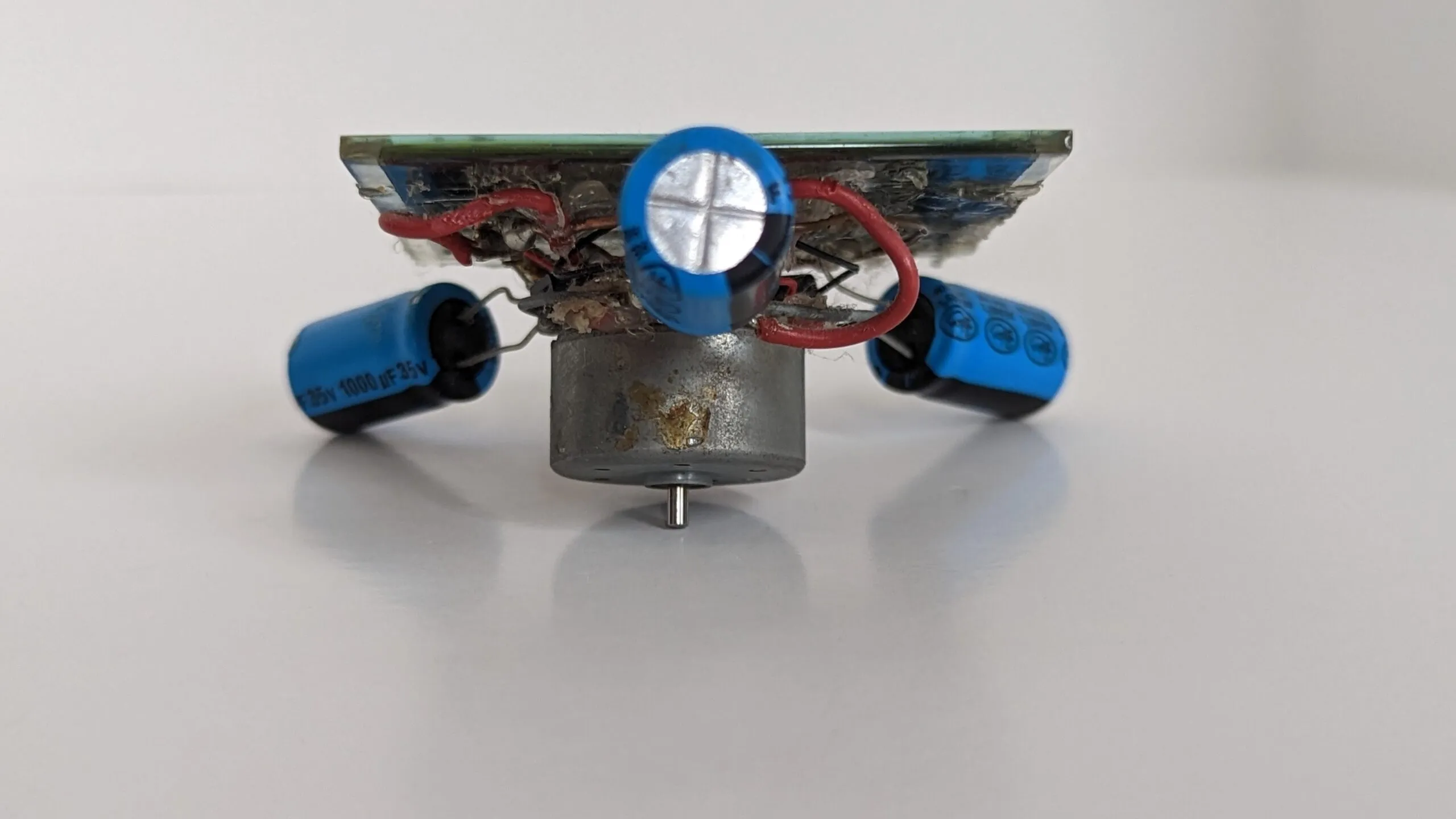 Underside of the Symet: the salvaged CD player motor hangs below the solar cell with the three capacitor feet angled out