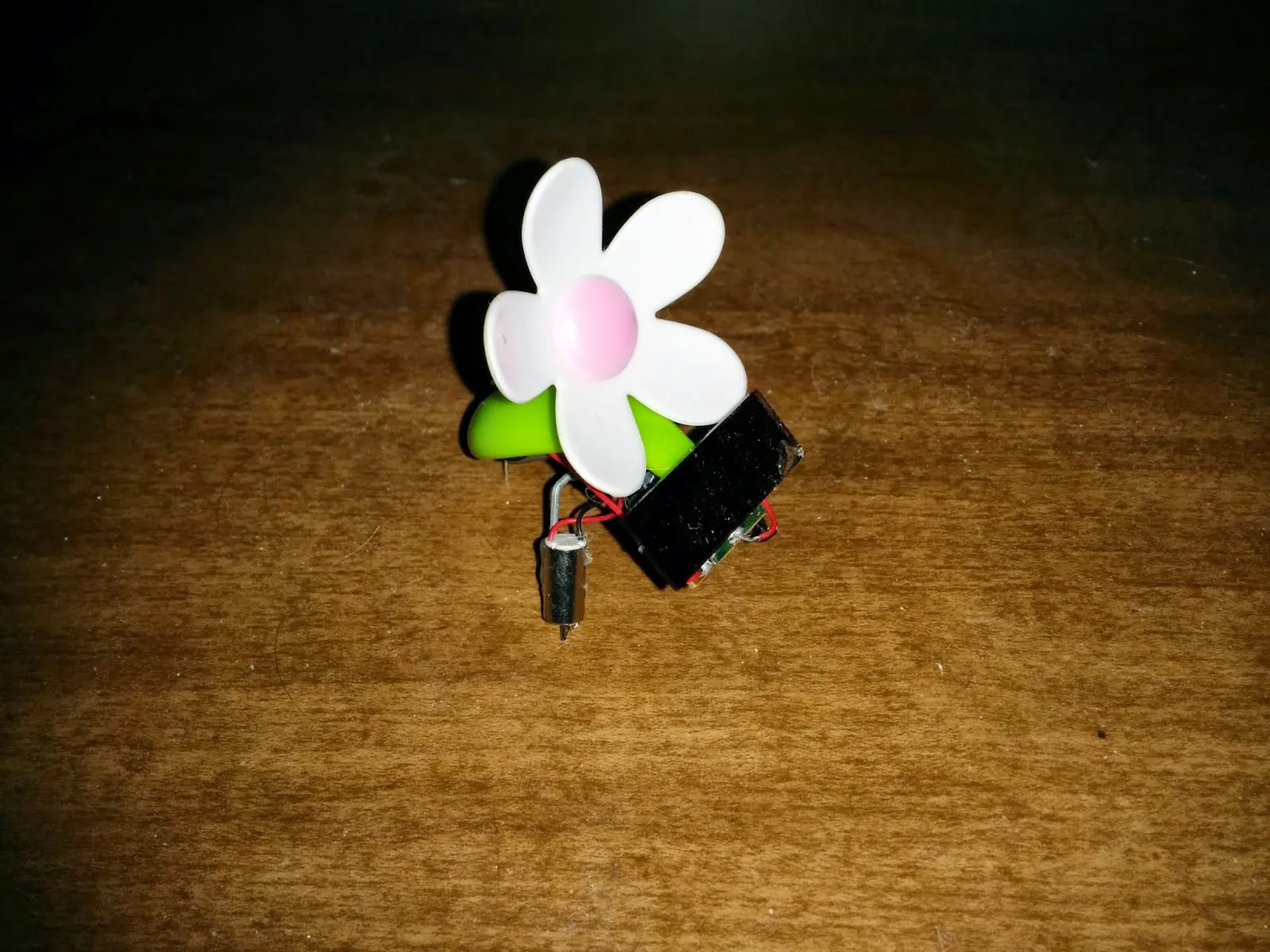 SymFlower v1: a plastic daisy on a green stem over a small solar panel, pager-motor foot below