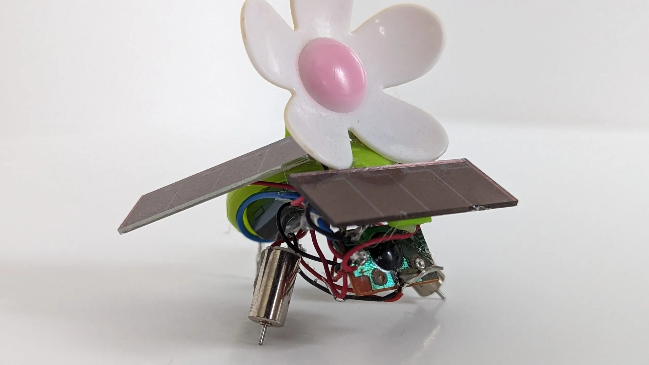 Close side view of SymFlower v2: mirrored solar wings spread under the daisy, twin pager motors as legs
