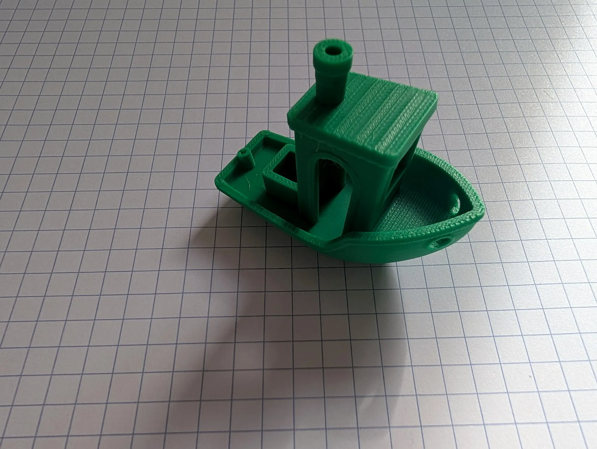 A green 3D printed Benchy boat on grid paper.