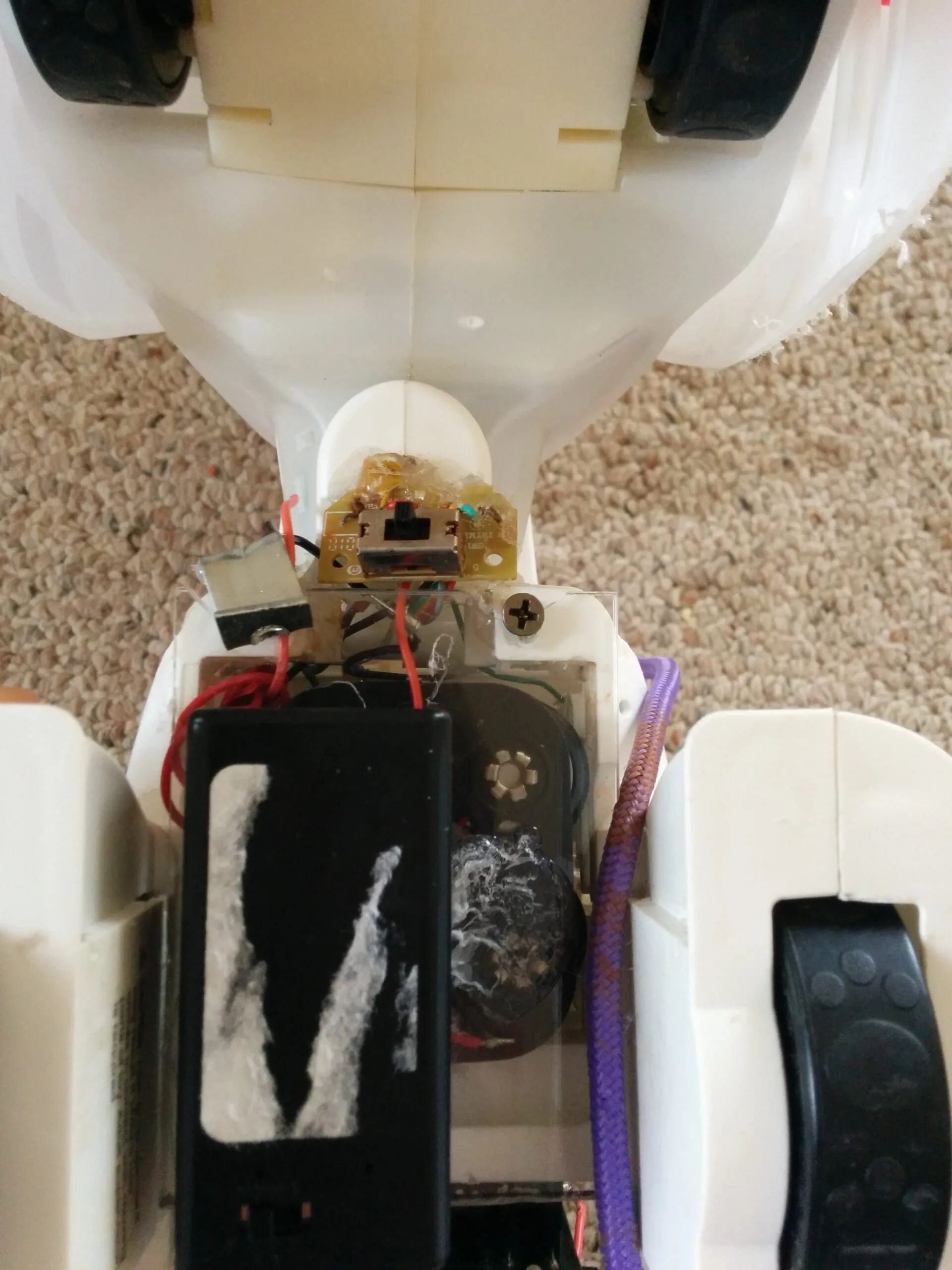 Bubbles' underside: the C battery holder, the relocated power switch hot glued in place, and a paw at the edge of frame