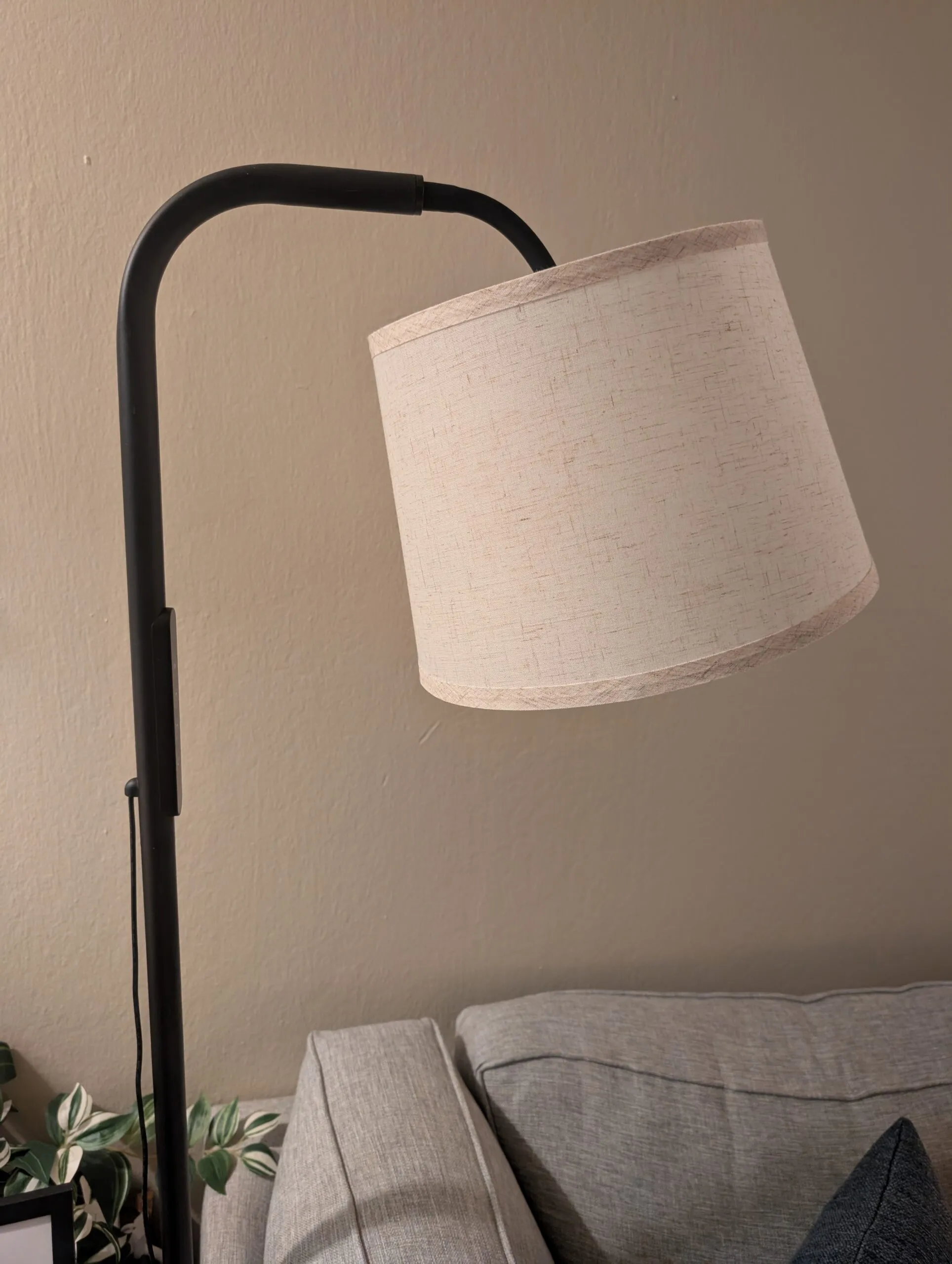 The SAD floor lamp: black arched arm with a linen drum shade, standing beside the couch