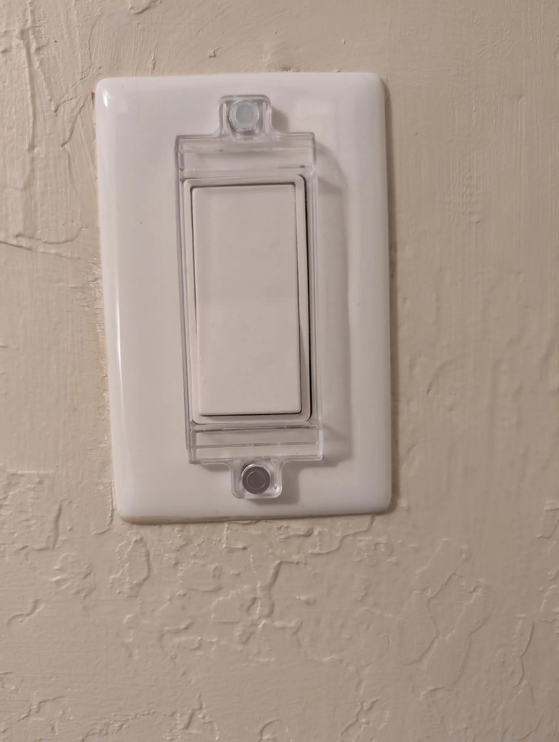 A wall rocker switch under a clear plastic guard held on by two magnets