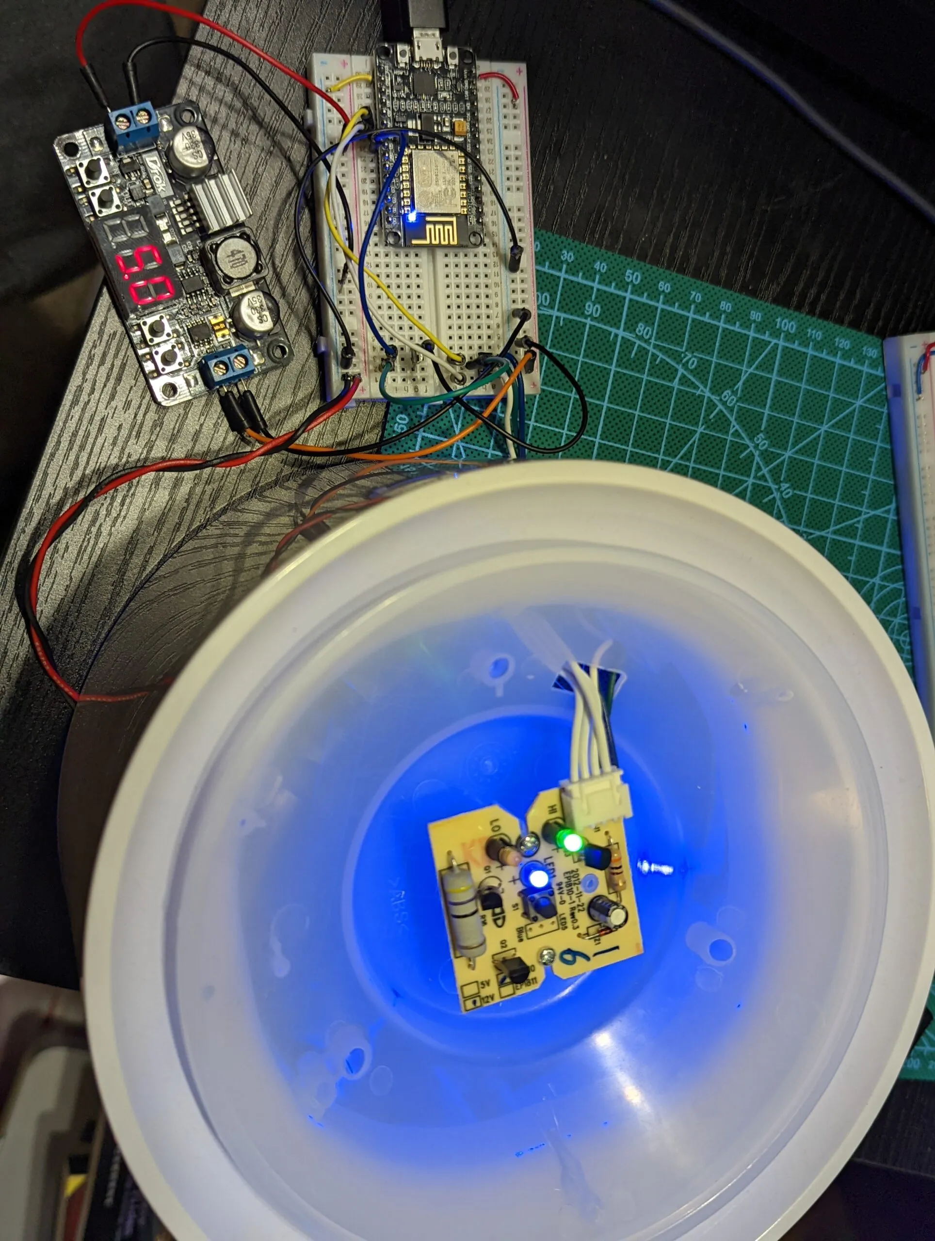 Bench test under power: buck converter reading 5.0 V, NodeMCU driving the control board, indicator LEDs lit inside the dome