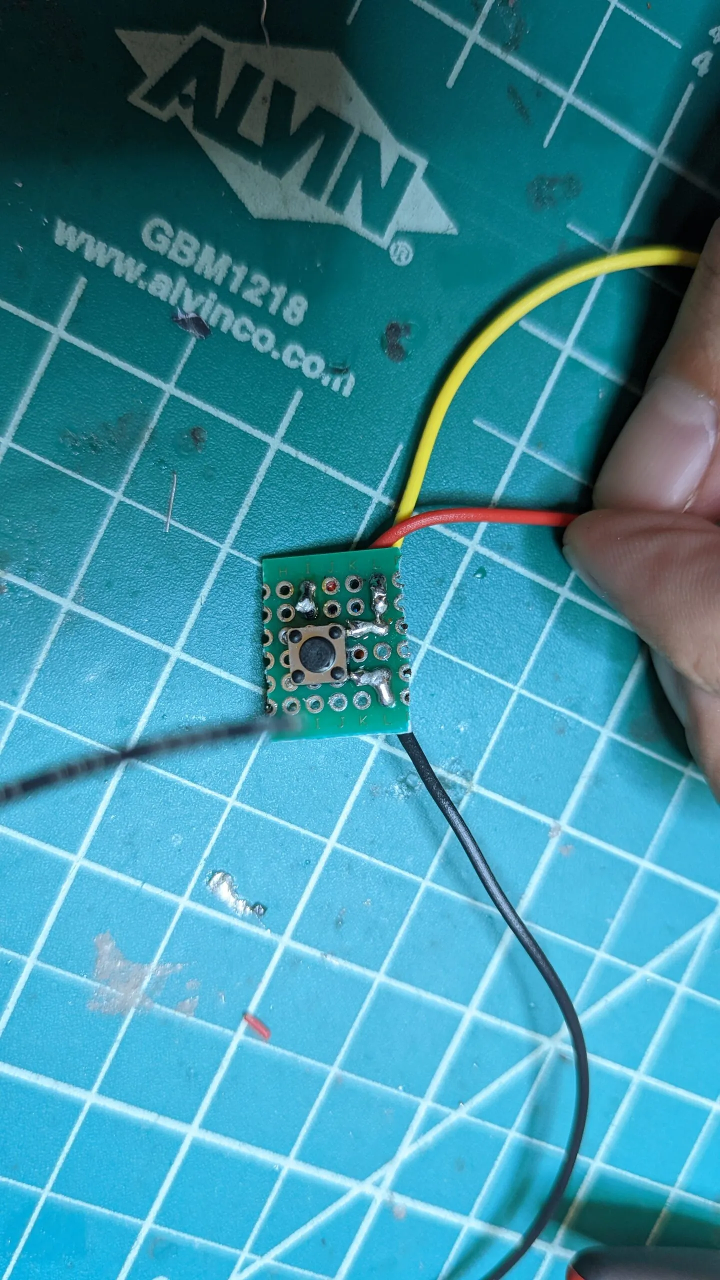 The reset button on a scrap of perfboard, three leads soldered out