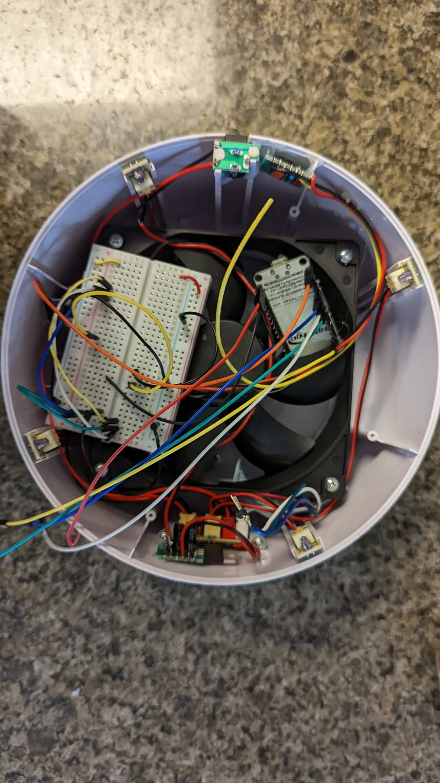 The breadboard resting in the shell on top of the fan, NodeMCU standing beside it, jumpers everywhere, halfway through moving the wiring over