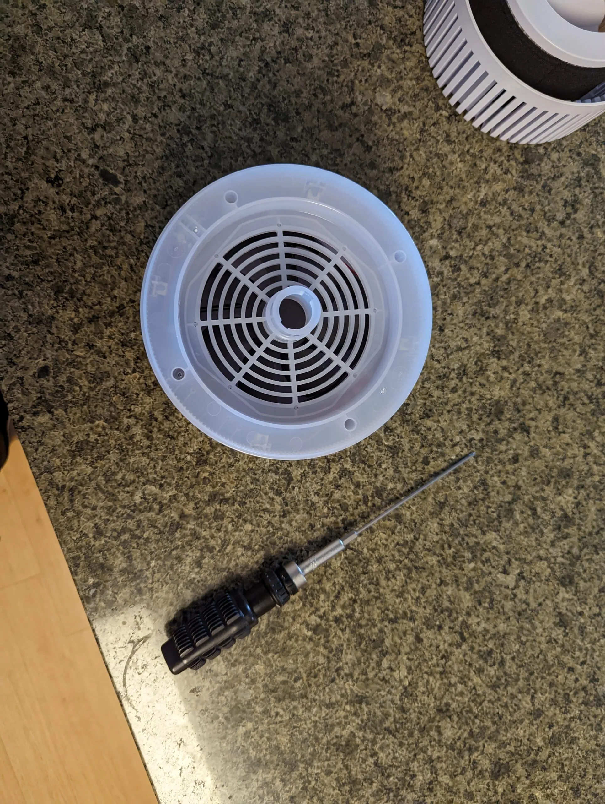 The grille plate off the bottom of the top half, its four deep screw holes visible, the long-bit driver on the counter and the filter cartridge behind