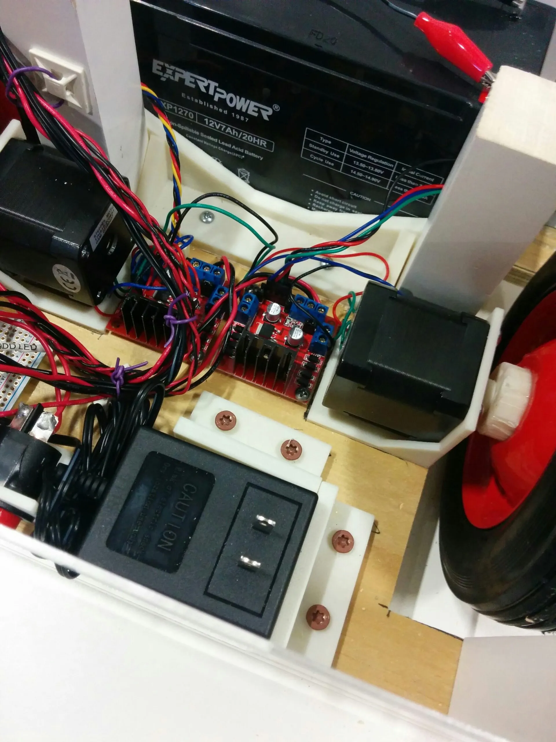 The power bay: 12 V 7 Ah SLA battery, onboard charger in a printed bracket, and the two rear L298N boards between the rear steppers