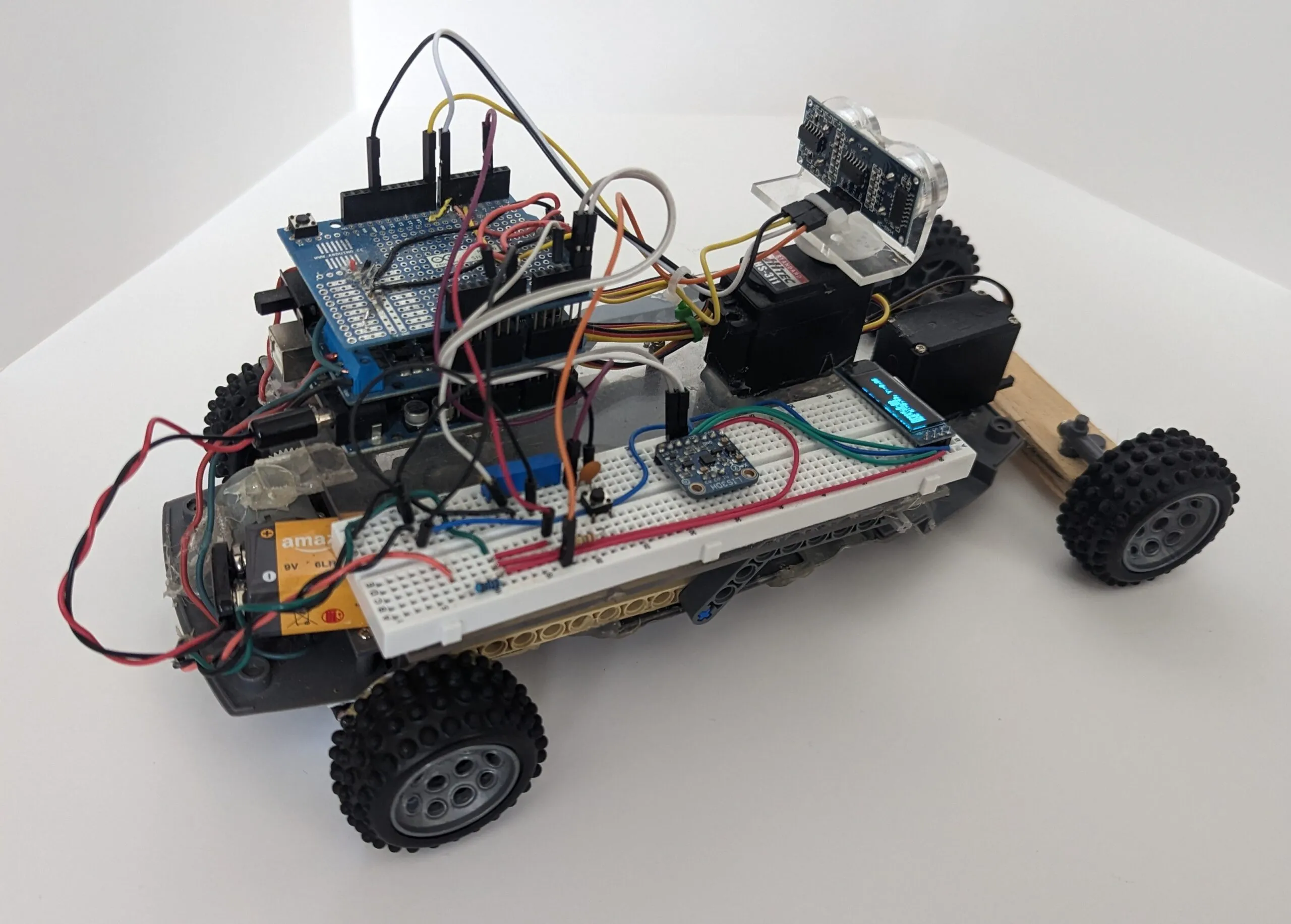 Three-quarter view of RoverBot: shield stack, breadboard with LIS3DH and OLED, servos back to the wooden axle