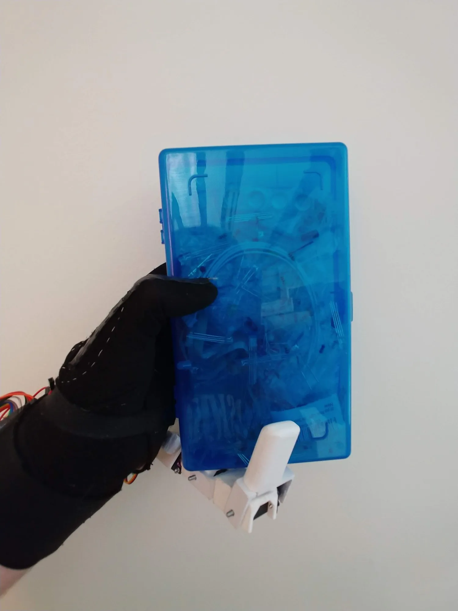 The gloved hand gripping a blue plastic case by its edge with the finger.