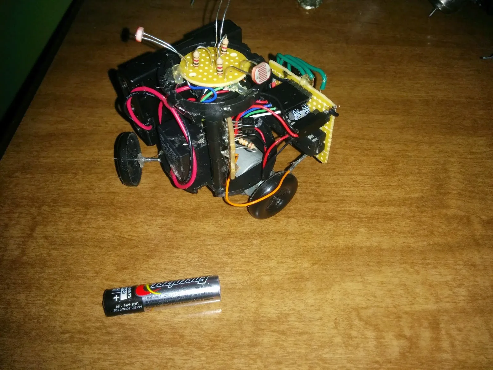 Triclops attempt 1 in 2014: photoresistor sensor disc atop a cylinder body, two of its three wheels visible, AAA battery for scale
