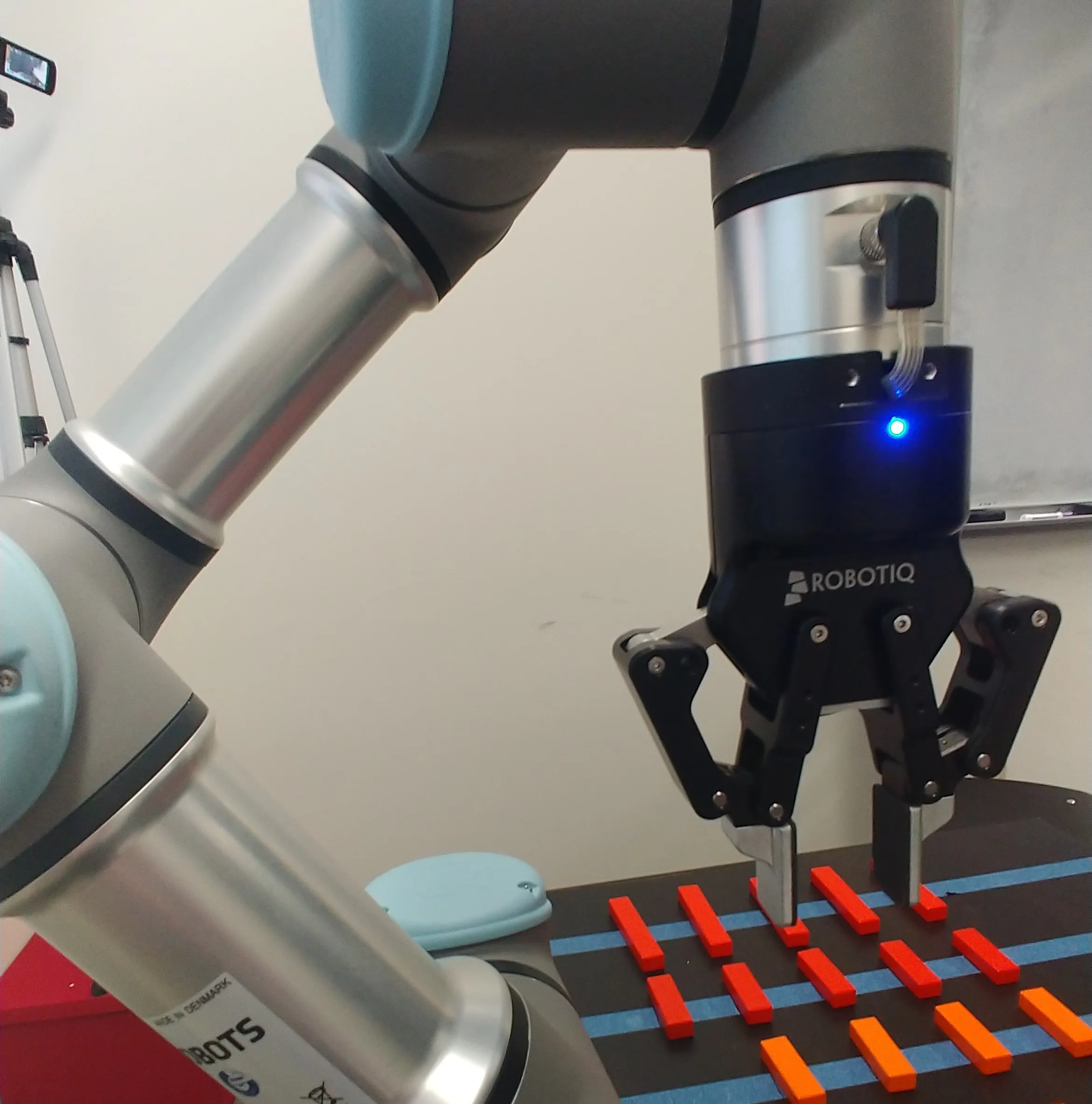 Close-up of the lab's UR3e arm with its Robotiq 85 gripper reaching over a table of small colored blocks